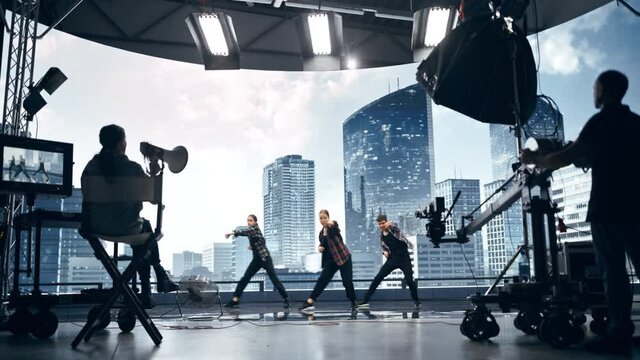 Music Clip Studio Set: Shooting Hip Hop Video Dance Scene with Three Professionals Dancers Performing on Stage with Big Led Screen with Modern City Background. Director and Cameraman in Backstage.