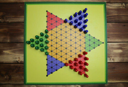 Top down view on isolated yellow gamboard with hexagon, multicolored game pieces, wooden background - chinese checkers (sternhalma)