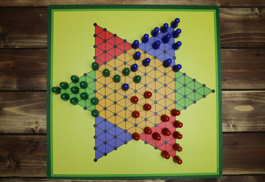 Top down view on isolated yellow gamboard with hexagon, multicolored game pieces, wooden background - chinese checkers (sternhalma)