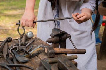 Professional blacksmith woman in historical costume working with metal on anvil at outdoor workshop...