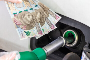 Fuel filler with inserted refueling gun and 500 zloty banknotes in hand, Concept of rising gasoline, oil and gas prices, close up