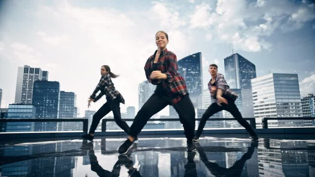 Diverse Group of Three Professional Dancers Performing a Hip Hop Dance Routine in Front of a Big Digital Led Wall Screen with Modern City Skyline with Office Skyscrapers in Studio Environment.