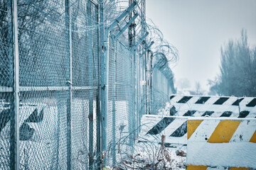 Barbed wire fence on border in winter. Concrete road blocks on ground. Closing for quarantine. Private object near highway. Maximum security detention facility. Unauthorized entry is prohibited.