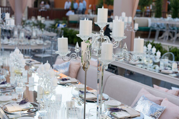 Beautiful decoration of a wedding banquet with a meal in the green garden in white colors. Very stylish setting with tropical flowers in a vase, glass candlestick set, napkins, plates, glasses cutlery
