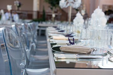 Beautiful decoration of a wedding banquet with a meal in the green garden in white colors. Very stylish setting with tropical flowers in a vase, glass candlestick set, napkins, plates, glasses cutlery