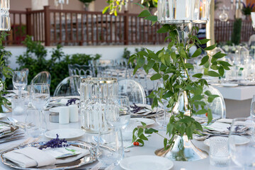 Beautiful decoration of a wedding banquet with a meal in the green garden in white colors. Very stylish setting with tropical flowers in a vase, glass candlestick set, napkins, plates, glasses cutlery