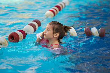 a funny little girl swims in inflatable armbands in a pool near the buoys. 