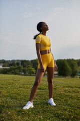 Athletic African-American woman in yellow fitness sports shirt and shorts standing in recovery after workout on hilltop 0654