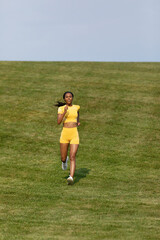 African-American woman in yellow fitness shirt and shorts runs down hill during her workout 0401