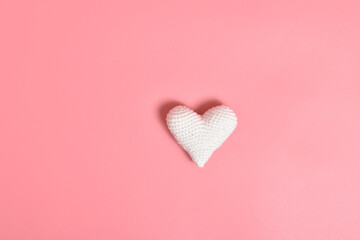 One white knitted heart lies on a pink background in the center. Background for Valentine's Day.