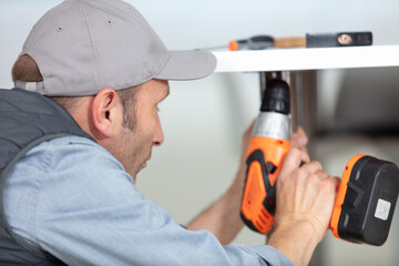 man holding a drill repairing a kitchen sink at home