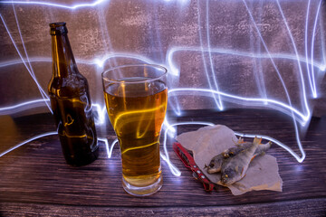 Beer with dried fish and opener on a wooden background with colorful lights.