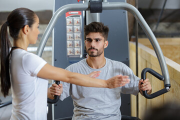 gym trainer showing how to use a machine to client