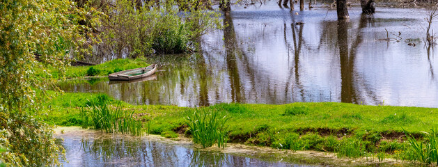 Spring landscape with a boat by the river and the reflection of trees in the water
