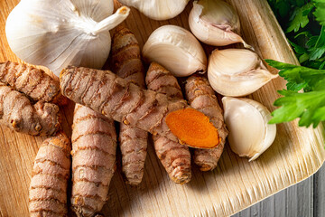 Raw organic curcuma roots and garlic cloves on a wooden plate close-up. Fresh whole turmeric rhizomes and garlic as spices, seasonings and natural antioxidants. Healthy eating ingredient. Top view.