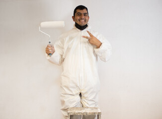 Pintor latino acabando de pintar pared blanca posa de frente a la cámara, saludando con actitud positiva.