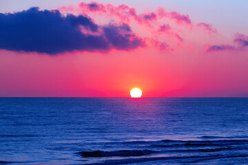 Stunning sunrise at Caspian Sea in Derbent, Dagestan. Sun disc over the horizon. Bright backlit sky and clouds. Silhouettes of waves in the rays of the sun. Incredible wallpaper