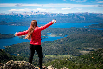 Mujer de campera roja admirando vista de los lagos de Bariloche desde cerro de gran altura