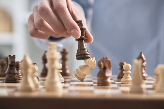 Man's hand holds a chess piece king. A dark colored chess piece. The figure flies. Chess game making a move by a player is an intellectual game.
