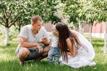 Fototapeta premium Happy young family, mom, dad and baby son spending time together outdoors in summer green garden