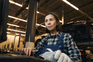 Fototapeta na wymiar Serious brunette woman in mechanic uniform looking puzzled at workplace
