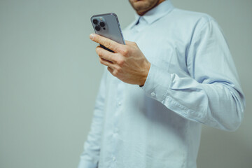 Close-up of a person in a light blue shirt using a smartphone. The individual's hands are gently holding the device, which features multiple camera lenses on the rear.