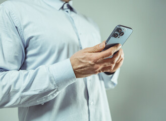 Close-up of a person in a light blue shirt using a smartphone. The individual's hands are gently holding the device, which features multiple camera lenses on the rear.