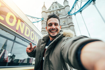 Smiling man taking selfie portrait during travel in London, England - Young tourist male taking...
