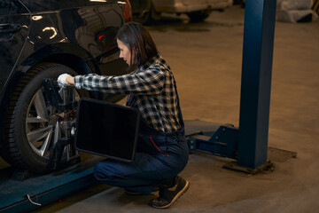 Capable brunette lady fixing a car tyre at service station