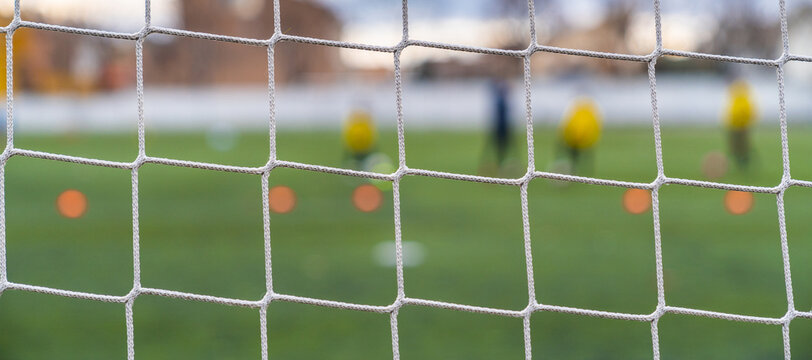 Soccer goal background with defocused green field. Closeup view, detail of the goal net. Amateur football game. Competition, football school.