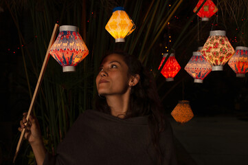 Hispanic young woman under a plant decorated with colorful paper lanterns while holding a stick...