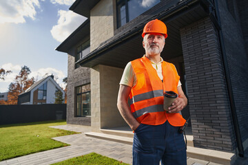 Mature construction worker with coffee before private house