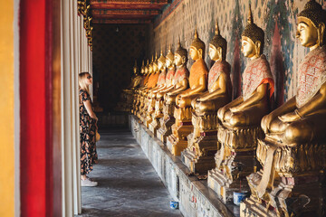 Fototapeta premium Blonde Touristin betrachtet Buddha Statuen in buddhistischem Tempel in Bagkok, Thailand