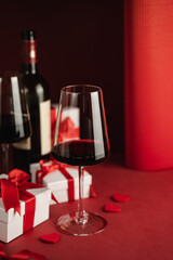 Two glasses and bottle of red wine, hearts, gifts boxes for Valentine day. Modern Still life. Red background. Greeting card for Valentine's Day
