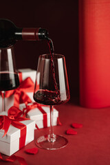 Two glasses and bottle of red wine, hearts, gifts boxes for Valentine day. Modern Still life. Red background. Greeting card for Valentine's Day