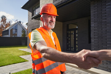 Aged worker giving handshake to house owner