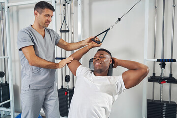 Male patient doing single-arm exercise guided by physiotherapist