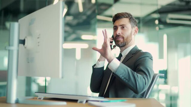 business confident man talking on cellphone sitting at desk in modern office. Caucasian male businessman worker in suit. Bearded successful employee entrepreneur working, communicating on mobile phone