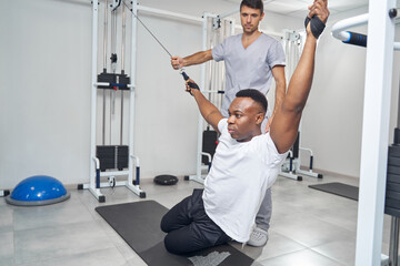 Concentrated man doing stretching exercise aided by physiatrist