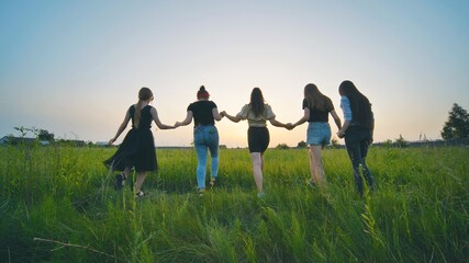 Fototapeta na wymiar Girls friends go hand in hand at sunset across the field.