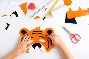 the process of making a children's New Year tiger mask with a child made of colored paper, top view, symbol 2022, step-by-step