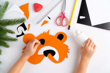 the process of making a children's New Year tiger mask with a child made of colored paper, top...