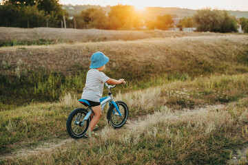 Fototapeta premium Side view of a caucasian boy in a blue hat riding the bike in a field. Healthy lifestyle.