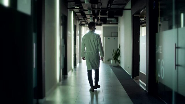 silhouette doctor walks down the empty corridor of a hospital or a modern clinic. Physician to go. Portrait of a serious confident medic therapist or surgeon going indoors hall