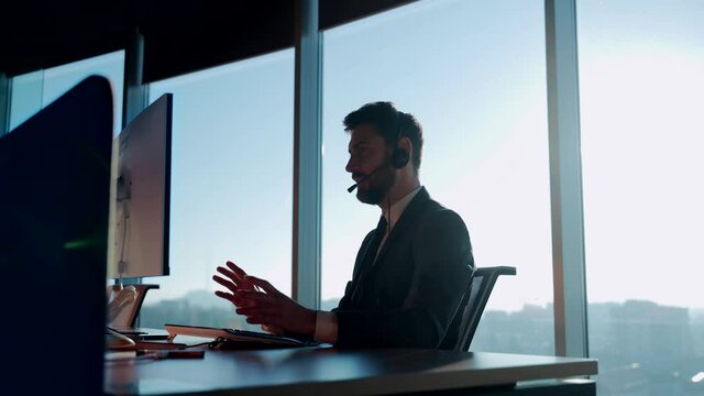 silhouette business man working in a modern office, online negotiations remotely. Male in suit on video call meeting, conference or helpline sitting at desk on computer and webcam at window background