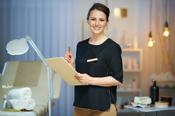smiling female worker with clipboard in modern beauty studio