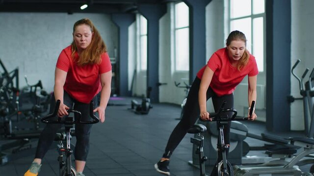 Class group of young women exercising on stationary cycling machine bike in gym. Modern sport activity, workout, healthy lifestyle. Athletic girls spinning bike, making tricks indoors. Slow motion