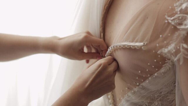 Bride's lace up dress. Bridesmaid tying bow on wedding dress. Woman's hands lace up on bride's corset. Bridesmaid ties and helps put on dress. Morning preparation of bride with white gown. Indoors