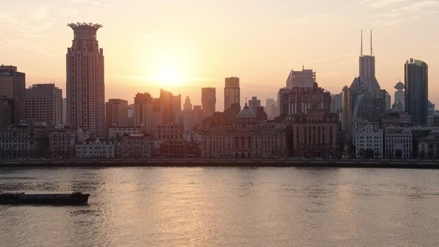 Time lapse footage of sunset in the Bund, historical landmark building skyline and Huangpu river, sun falling behind buildings with ships sailing on river, 4k video.