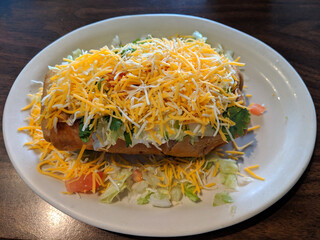 Chimichanga covered in sour cream, Cheese, lettuce and tomatoes